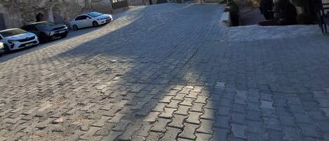Una calle adoquinada en un pueblo histórico con edificios de piedra, coches aparcados y cielo despejado.