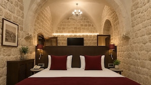 A hotel room with a stone wall, a chandelier, a bed with red and white bedding, and a flat-screen TV.