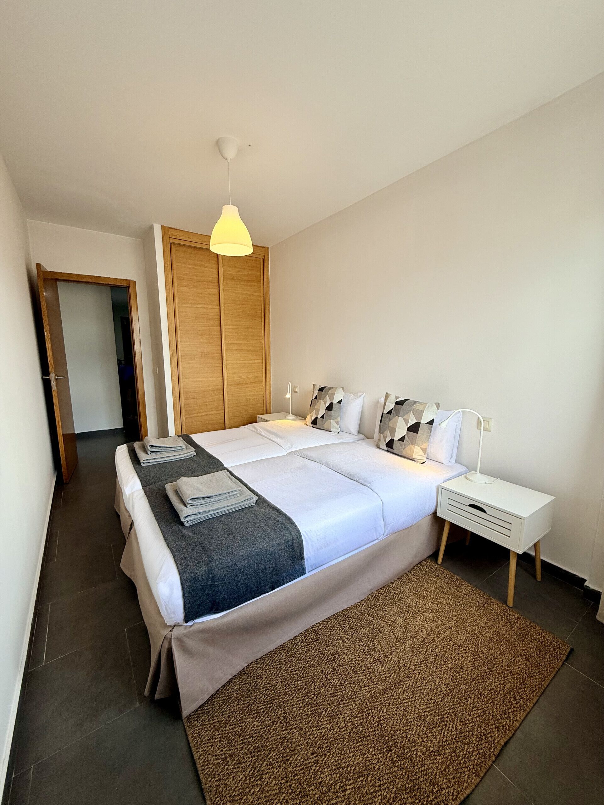 Un dormitorio con cama, mesita de noche, lámpara y armario.