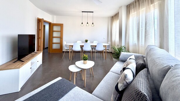 A modern living room with a sofa, TV, dining area, and ceiling fan. - Dragos Suites 204 (Arrecife)