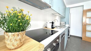 A modern kitchen with a built-in stove, a sink, and a toaster. There is a woven basket with yellow flowers on the counter. - Dragos Suites 204 (Arrecife)