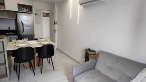 Una cucina moderna con frigorifero, tavolo da pranzo apparecchiato con piatti e bicchieri, e un divano grigio.