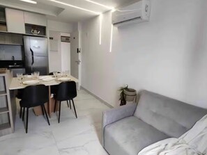 A modern kitchen with a refrigerator, dining table set with plates and glasses, and a grey sofa. - Hermano 504 · Modern apartment 300 meters from Bessa beach (João Pessoa)