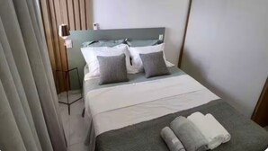 Una camera d'albergo con un letto, cuscini, un comodino, un condizionatore d'aria e una tenda.