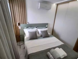 A hotel room with a bed, pillows, a bedside table, an air conditioning unit, and a curtain. - Hermano 504 · Modern apartment 300 meters from Bessa beach (João Pessoa)
