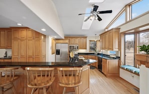 Una cocina moderna con armarios de madera, una isla central con taburetes y un ventilador de techo, además de un ventanal grande.