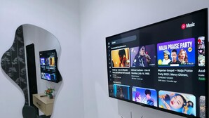 Habitación moderna con televisor de pantalla plana mostrando videos musicales, un espejo, un escritorio con un control remoto y una silla.