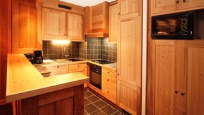 A kitchen with wooden cabinets, a black tiled backsplash, a built-in oven, and a microwave. - Spacious Alpine Apartment by the Chairlifts (Les Deux Alpes)