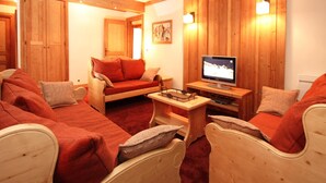 A cozy room with wooden walls, a sofa, a chair, a small table, and a television. - Spacious Alpine Apartment by the Chairlifts (Les Deux Alpes)