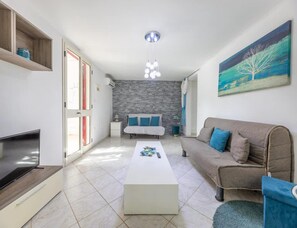Un salon moderne avec un canapé, une table basse, un téléviseur, un mur en pierre et un tableau.