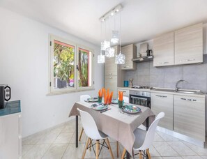 Eine moderne Küche mit Essbereich, einem Fenster mit Blick auf Grünflächen und einem für zwei Personen gedecktem Tisch.