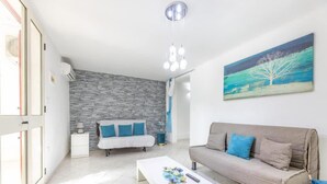 Een moderne woonkamer met een stenen muur, een witte bank, een grijze bank, een witte salontafel en een schilderij aan de muur.