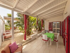 Eine überdachte Terrasse mit Tisch, Stühlen und einer Sitzecke, mit Blick auf den Garten.