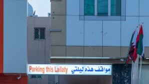 Ein Gebäudeeingang mit einem mehrsprachigen Schild, darunter auch Arabisch, und einer Flagge.