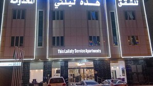 Ein Gebäude mit beleuchteter Beschilderung in Arabisch und Englisch, das als Serviced-Apartment-Komplex gekennzeichnet ist.