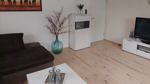 A living room with a sofa, a coffee table with salt and pepper shakers, a TV on a stand, a white cabinet, a vase with branches, and a painting of giraffes. - Vacation apartment on the edge of the Sauerland and the border of the Ruhr area (Wickede (Ruhr))