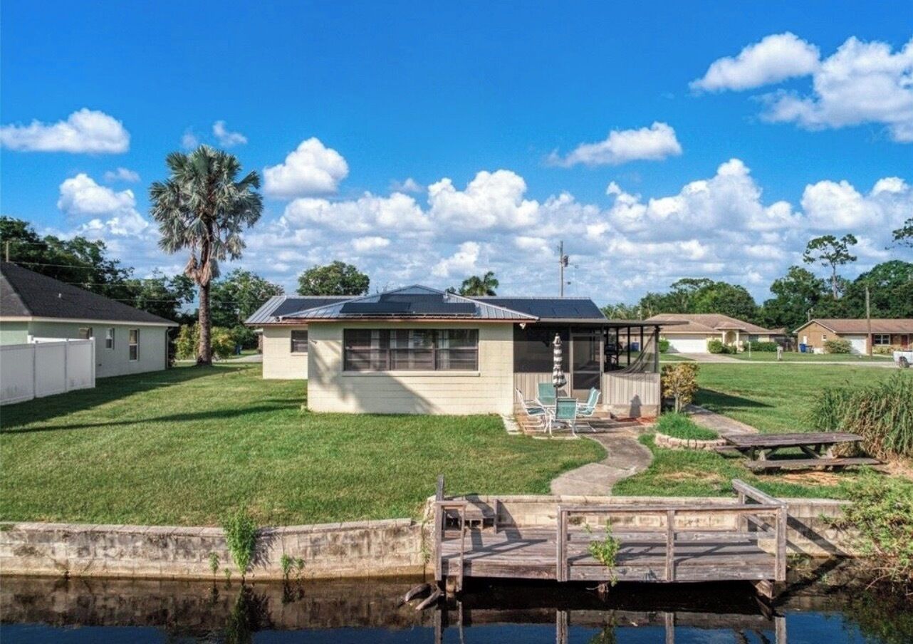 A single-story house with a covered patio, a small deck, and a pond in the foreground.