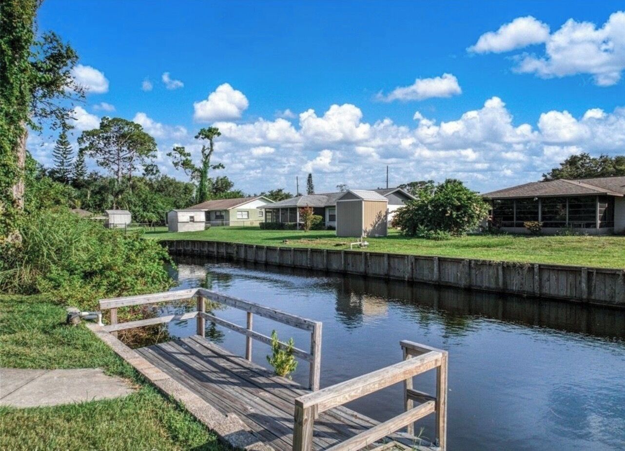 A canal-side property with a wooden dock, a grassy area, and a building with a sloped roof.