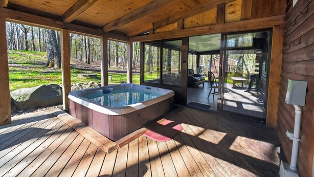 Un patio di legno con una vasca idromassaggio, ampie vetrate che si aprono su un portico esterno arredato.