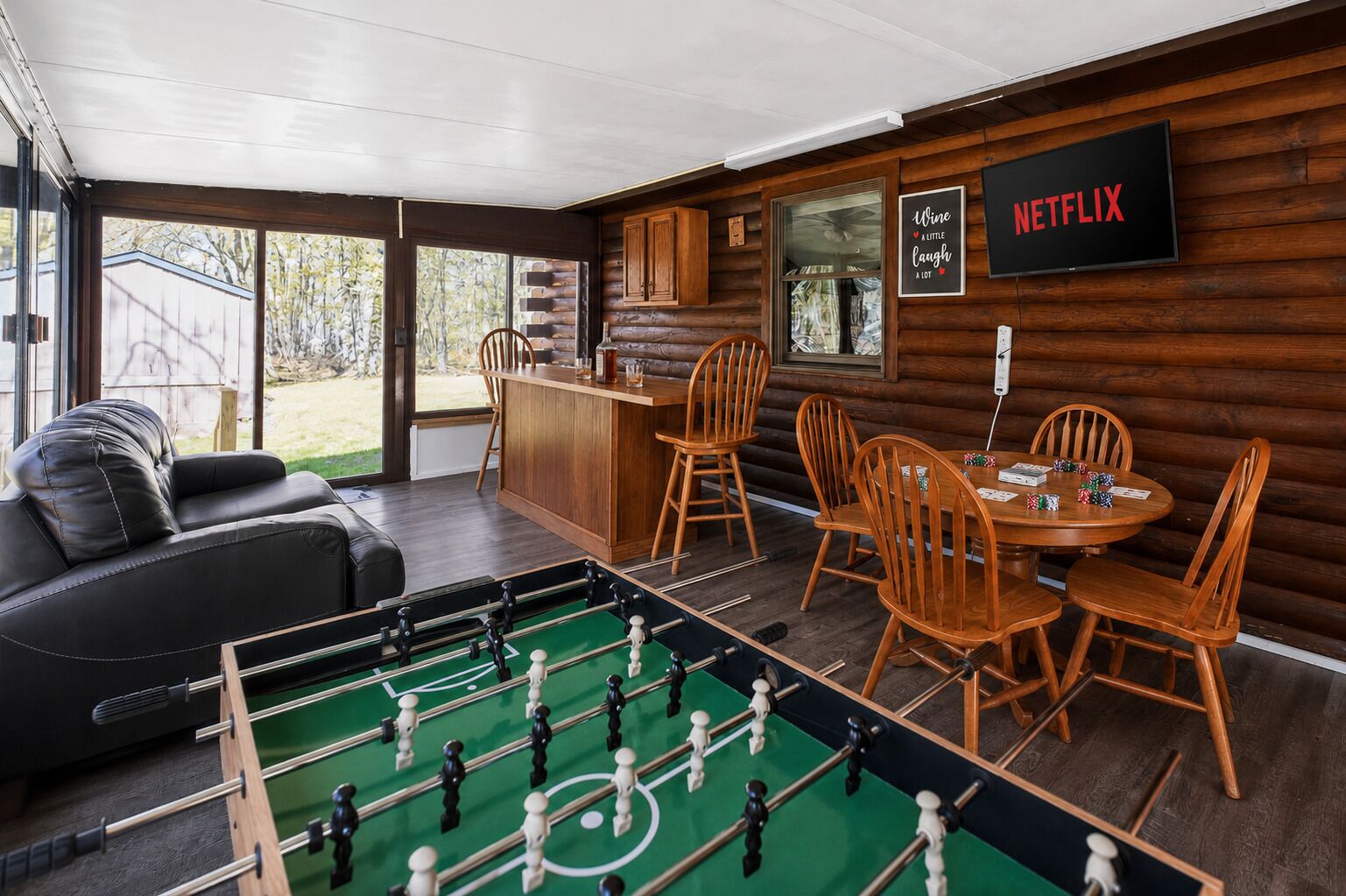 Ein gemütliches Zimmer mit einem Kicker, Holzsesseln, einer Bar und einem Fernseher, der 'NETFLIX' zeigt.