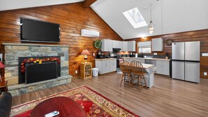 Un ampio soggiorno mansardato con camino, televisione, cucina dotata di elettrodomestici moderni e zona pranzo.