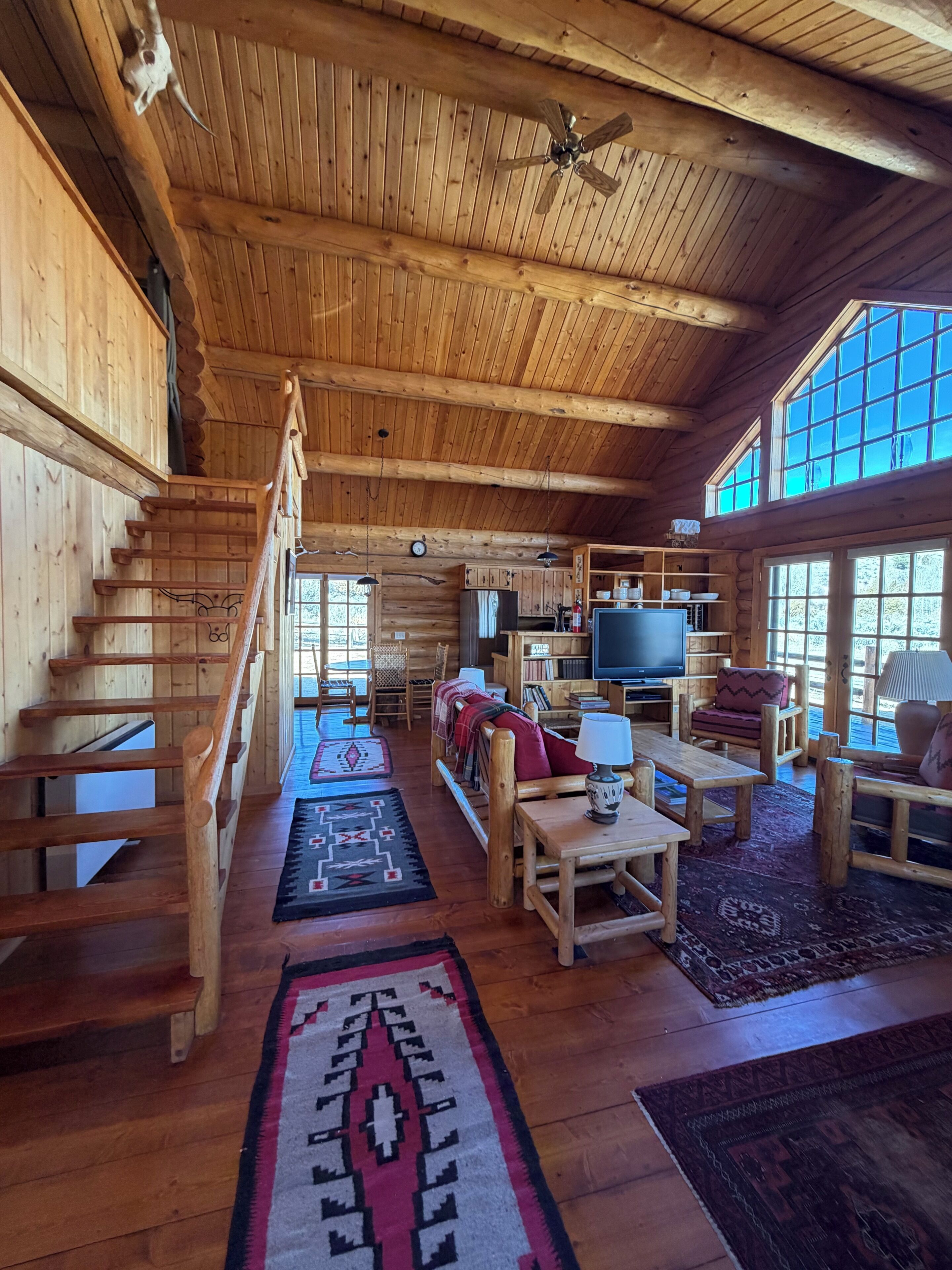 L’intérieur d’un chalet en bois comprend un escalier, un téléviseur, un canapé et un coin repas.