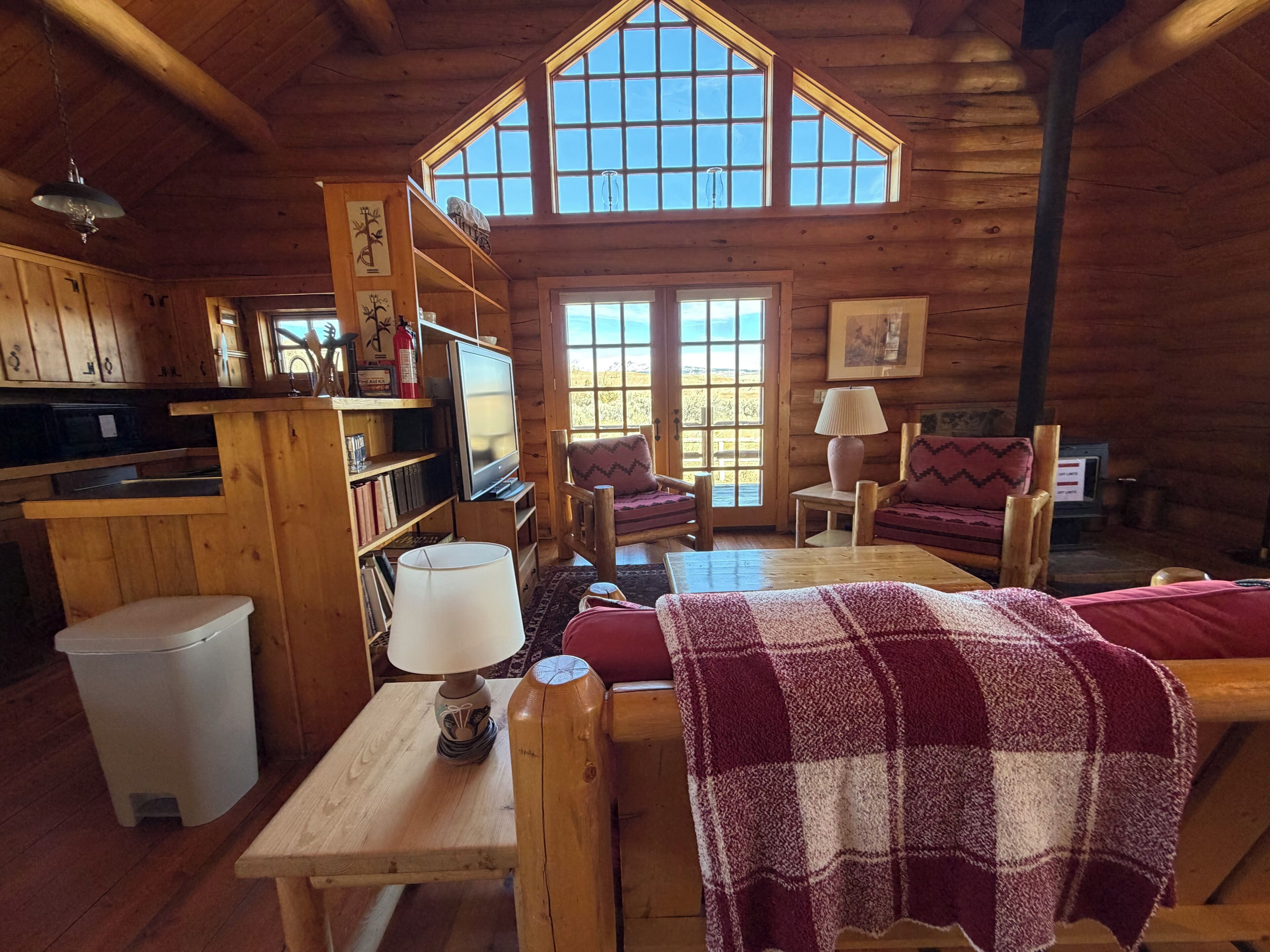 L’intérieur chaleureux d’un chalet, avec un décor en bois, une télévision, une cheminée et une grande fenêtre.
