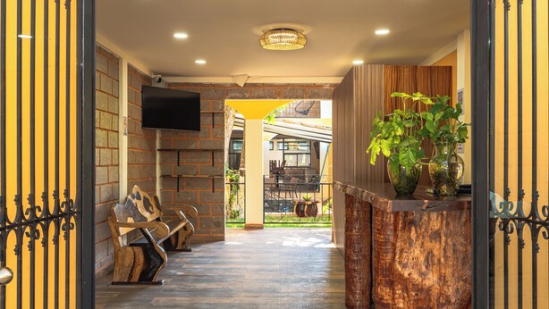 A hallway with a wooden floor, a reception desk with a plant, a television mounted on the wall, and a staircase leading to an outdoor area.