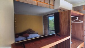 A room with a bed, a wooden bench, a hanging clothes rack, and a brick wall design.