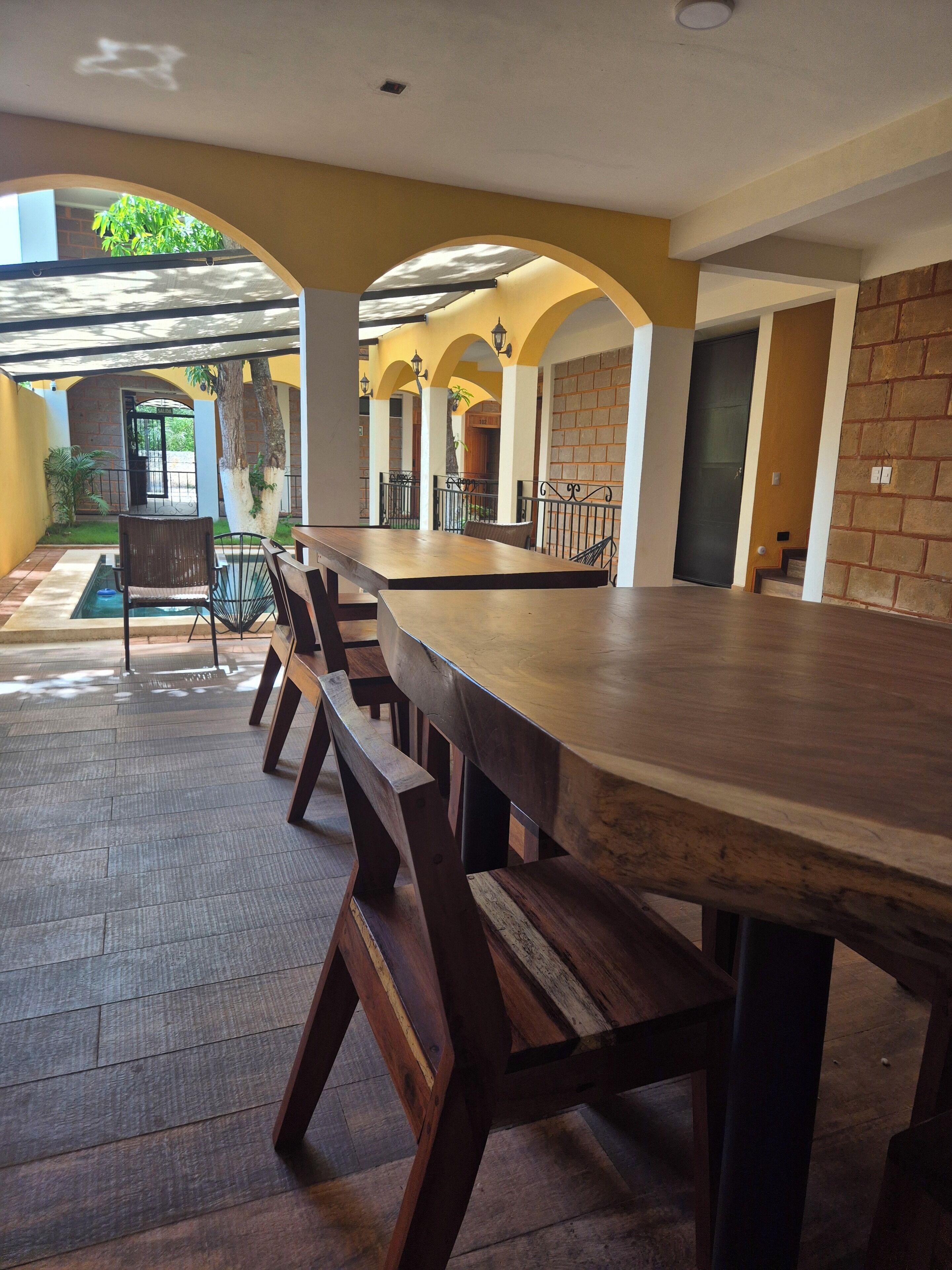 A long wooden table with benches in a covered outdoor area with a brick wall and arched ceiling.