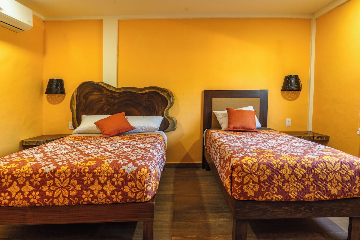 Ein Hotelzimmer mit zwei Betten, jeweils mit gemusterten Tagesdecken, Holz-Kopfteilen und Wandleuchten.