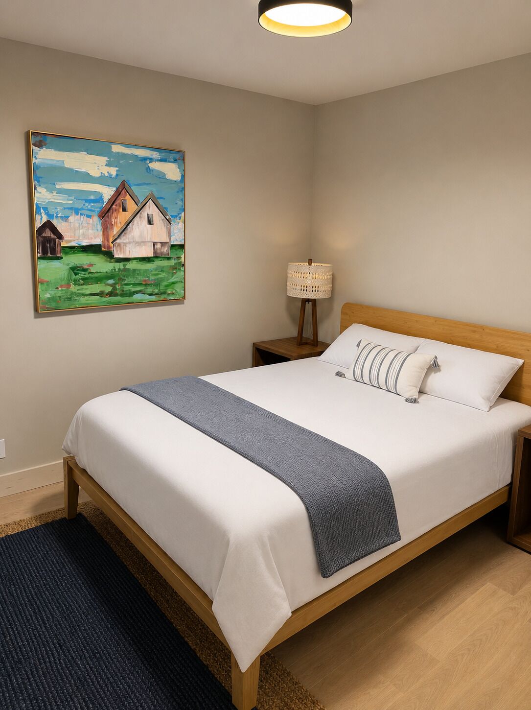 Un dormitorio con cama, mesita de noche, lámpara y un cuadro en la pared.
