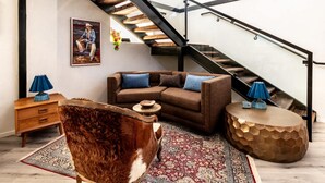 Ein Wohnzimmer mit einer Couch, einem Couchtisch, einem Teppich, einem Hund, einer Treppe und einem Gemälde an der Wand.