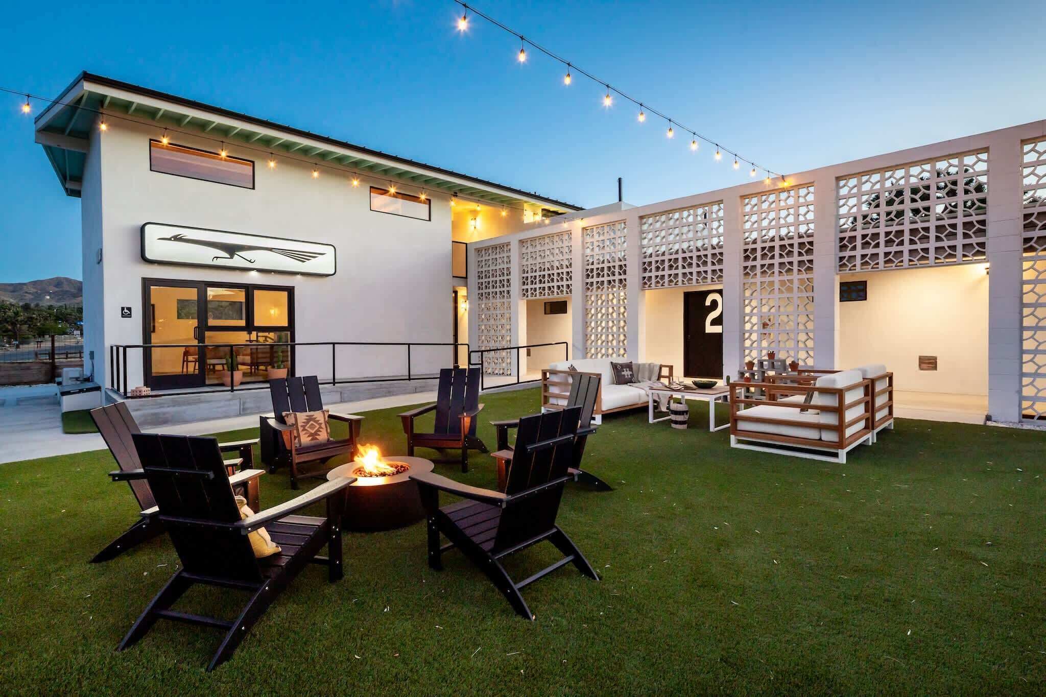 A modern outdoor patio with a fire pit, lounge chairs, and a white building with a number '2' sign.