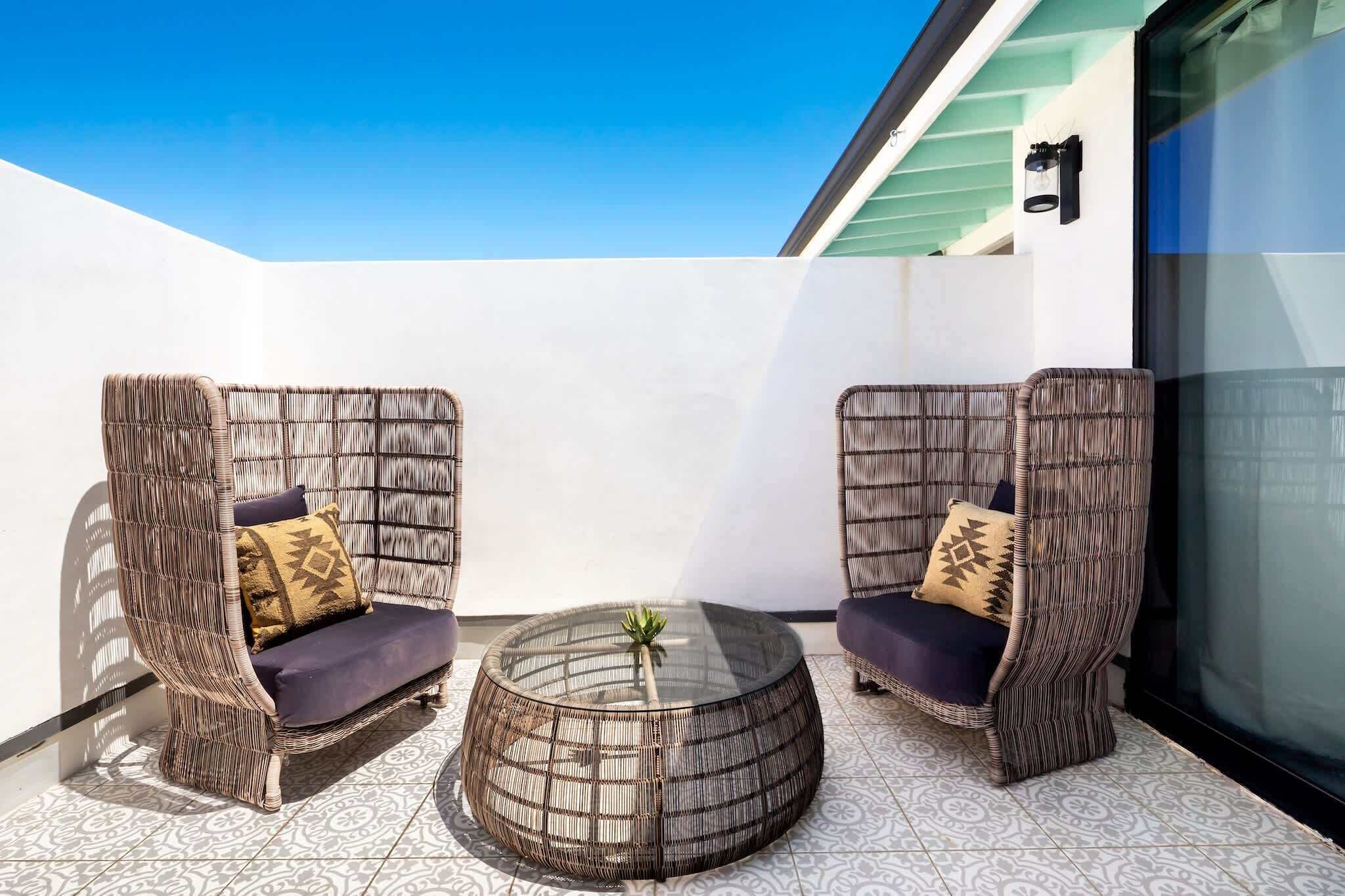 A modern outdoor seating area with wicker chairs and a glass coffee table.