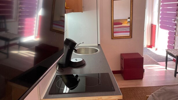 Una habitación de hotel moderna con televisión de pantalla plana, cafetera, placa de cocción por inducción integrada, una caja roja de almacenamiento y un cuadro en la pared.