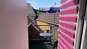 Un pequeño patio al aire libre con una mesa y dos sillas, barandilla de metal y una puerta que da a un edificio.