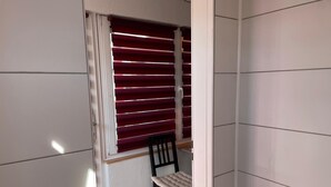 Una habitación con ventana, persianas horizontales, una silla y un armario blanco.