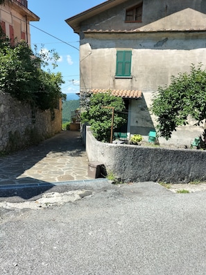 Uma rua estreita com um edifício que apresenta uma parede de pedra, uma janela verde e um telhado em telhas.