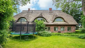 A house with a thatched roof, brick walls, and a trampoline in the yard. - Apartment "Kastanie" with Private Outdoor Terrace in the Garden (Putbus)