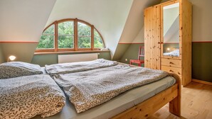 A bedroom with a loft-style ceiling, a wooden wardrobe, two beds with patterned bedding, a window with a view of greenery, and a radiator. - Apartment "Kastanie" with Private Outdoor Terrace in the Garden (Putbus)