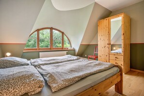 A bedroom with a loft-style ceiling, a wooden wardrobe, two beds with patterned bedding, a window with a view of greenery, and a radiator. - Apartment "Kastanie" with Private Outdoor Terrace in the Garden (Putbus)