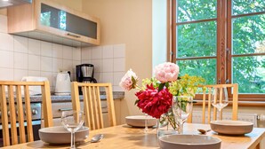 A kitchen with wooden cabinets, a dining table set with bowls and wine glasses, and a window with a view of greenery. - Apartment "Kastanie" with Private Outdoor Terrace in the Garden (Putbus)