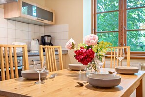 A kitchen with wooden cabinets, a dining table set with bowls and wine glasses, and a window with a view of greenery. - Apartment "Kastanie" with Private Outdoor Terrace in the Garden (Putbus)