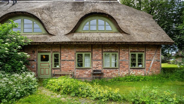 A rustic brick house with a thatched roof, green-framed windows, and a wooden door. - Apartment "Kastanie" with Private Outdoor Terrace in the Garden (Putbus)