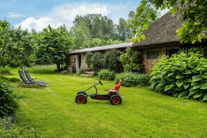 Un jardin verdoyant avec une tondeuse à gazon, deux chaises longues et une maison au toit de chaume.