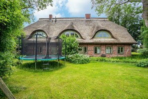 Une maison avec un toit de chaume, des murs en briques et un trampoline dans la cour.