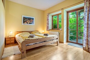 A bedroom with a wooden bed, a nightstand, a lamp, a radiator, and a window with curtains. - Apartment "Laubfrosch" with Private Outdoor Terrace in the Garden (Putbus)