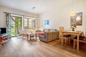 Un vaste espace de vie comprenant un canapé, une table à manger et des chaises, de grandes fenêtres avec des rideaux et un téléviseur.