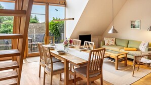 A dining area with a wooden table and chairs, a sofa, and a view of the outdoors. - Apartment "Waldkauz" with Private Balcony (Putbus)